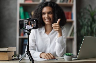 Beyaz tişörtlü Afrikalı Amerikalı kadının sosyal ağları için yeni video blogu kaydederken bulanık bir geçmişi var. Modern akıllı telefonun kamera ekranına odaklan.