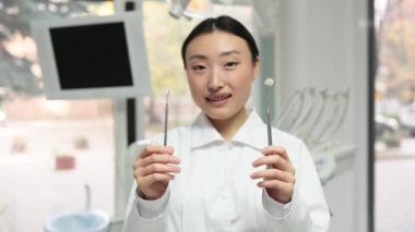 Modern tıbbın arka planında duran mutlu genç bayan Asyalı dişçi aletleriyle ellere odaklan. Halk, tıp, stomatoloji ve sağlık hizmetleri kavramı.