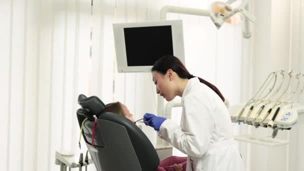 从侧面看身穿白衣戴手套的漂亮的亚裔医生 为她那可爱的小女孩做检查或治疗龋牙痛 坐在牙椅上 — 图库视频影像