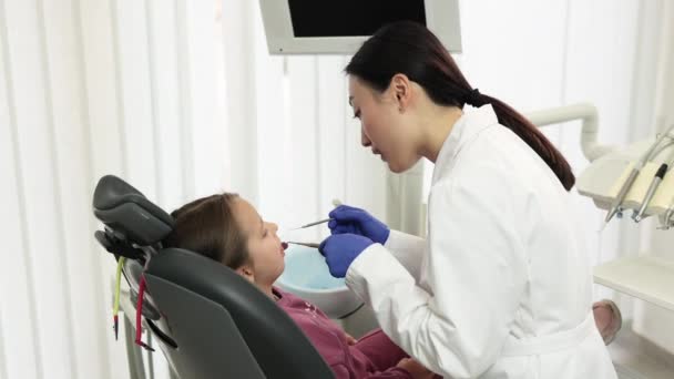从侧面看身穿白衣戴手套的漂亮的亚裔医生 为她那可爱的小女孩做检查或治疗龋牙痛 坐在牙椅上 — 图库视频影像