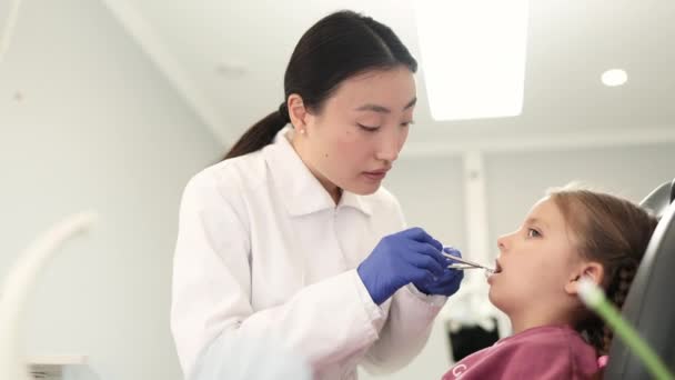 美丽的笑与白色的牙齿 亚洲牙医在牙科诊所用放大镜检查一个年轻漂亮女孩的口腔 — 图库视频影像