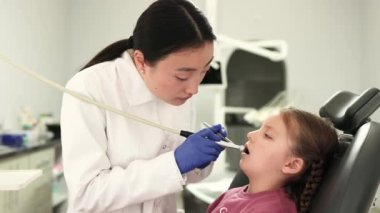 Modern Çocuk Diş Kliniği 'nde dişçilik yaparken çok tatlı bir kız. Asyalı bir dişçi, diş ve ayna kullanarak bir kızın dişlerini tedavi ediyor..