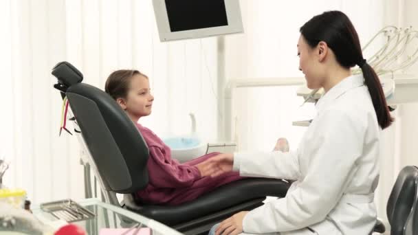 在现代明亮的诊所里 笑容满面的小高加索儿童患者在成功且无痛的牙科治疗之后 与亚洲牙医握手 儿科口腔学概念 — 图库视频影像