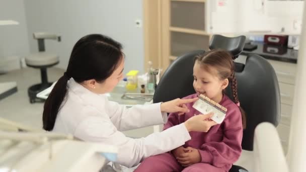 Asiatisk Tandläkare Kontrollera Och Välja Färg Unga Kaukasiska Flickor Tänder — Stockvideo