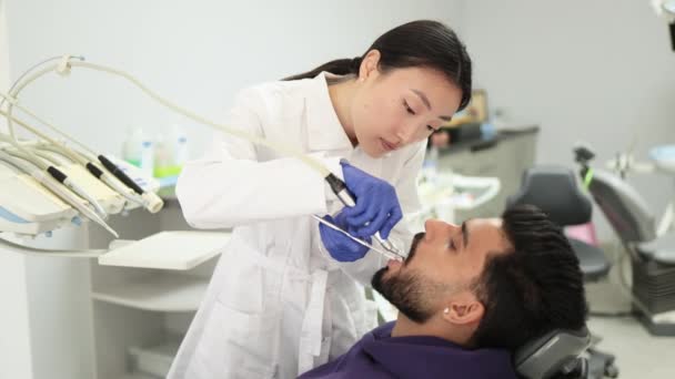 愉快的病人和牙医的概念 年轻美丽的亚洲女口腔学家用牙钻治疗一个英俊的长胡子小伙子的牙齿 口腔卫生 — 图库视频影像