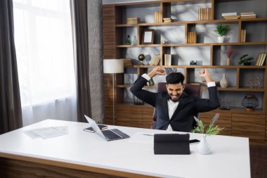 Heyecanlı genç sakallı iş adamı ya da bilgisayar ve tabletle çalışan girişimci ellerini kaldırarak zafer kazandı çünkü başarılı bir iş anlaşması yaptık..