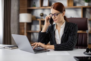 Resmi çağrı. Gözlüklü, kendine güvenen genç ve güzel bir kadın iş ortaklarını arıyor, yeni anlaşma hakkında konuşuyor ve soruyor, modern ofiste dizüstü bilgisayarla çalışıyor..