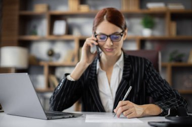 İş, teknoloji, iletişim ve insan konsepti - mutlu gülümseyen beyaz iş kadını masasında oturmuş modern ofisteki telefon eden kağıtlarla.