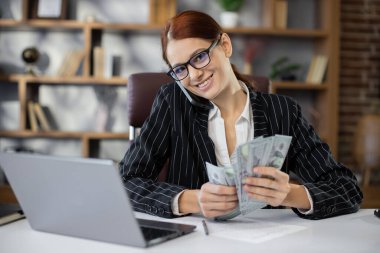 Rich business woman working on smartphone counting money cash, calculate earnings income profit at office workplace. Professional manager freelancer girl. Business people. Employment, occupation