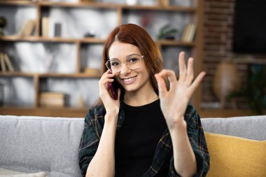 Kafkas kökenli genç bir kadının portresi yakın çekyatta, elinde modern akıllı telefonuyla oturuyor ve tatilde müşterilere sesleniyor. Güzel bir bayan iş günü evde dinleniyor ve işaret veriyor.