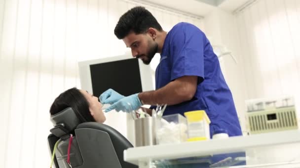 身穿白衣戴手套 留着胡子的男医生的侧视图 为他的女病人做检查或治疗龋和牙痛 这位年轻的亚洲女人坐在牙椅上很有魅力 — 图库视频影像