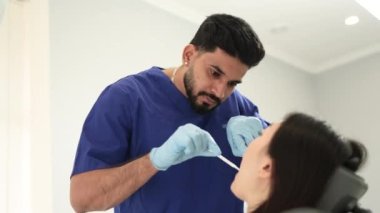 Kadın hastanın düşük açılı görüntüsü, dişçi koltuğunda oturan çekici genç Asyalı kadın, beyaz üniformalı ve eldivenli sakallı erkek doktor, muayene ediyor veya diş ağrısını tedavi ediyor..