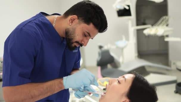 美丽的笑与白色的牙齿 年轻自信的牙医通过牙科诊所的放大镜检查漂亮美女的口腔 — 图库视频影像