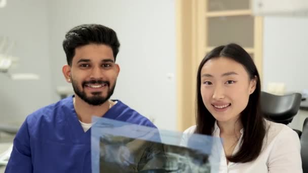 微笑着快乐的亚洲女人拜访牙医 坐在现代轻医院诊所的牙科椅子上 年轻的满脸胡须的牙医拿着显示大拇指的X光图像扫描 — 图库视频影像