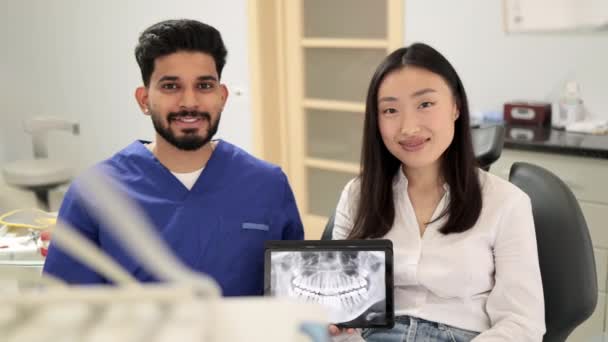 Uśmiechnięta Azjatka Odwiedzająca Pewnego Siebie Brodatego Dentystę Siedząca Krześle Dentystycznym — Wideo stockowe