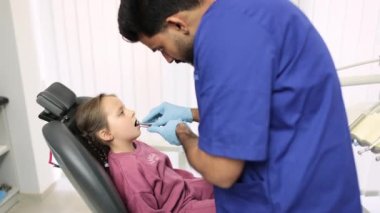 Modern Çocuk Diş Kliniği 'nde dişçilik yaparken çok tatlı bir kız. Çekici erkek sakallı dişçi bir kızın dişlerini tedavi ediyor, diş matkabı ve ayna kullanıyor..