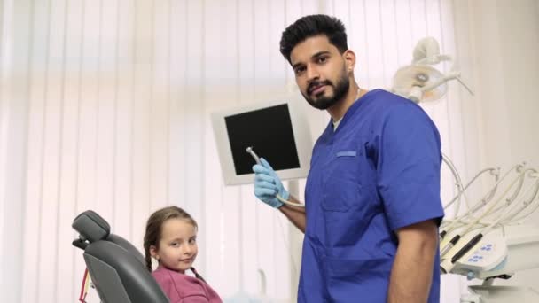 儿童的牙齿治疗 在轻盈的现代牙科诊所里 坐在牙医椅子上笑着的小女孩 并兴奋地看到自信的男牙医竖起大拇指 看着相机 — 图库视频影像
