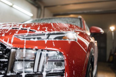 Araba yıkama servisinde araba farı yıkıyorum. Sabunlu kırmızı araba. Aktif temizlik köpüğüyle çapraz araba yıkama, araba sabunlu kaputunun ön görüntüsü..