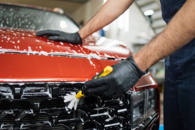 Kırmızı ızgarayı temizleyen özel sarı temizlik işçisi fırçasıyla bir araç temizleme atölyesinde el görüntüsü. Otomobil hizmet endüstrisi.