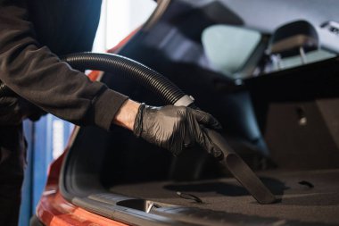 Arabanın bagajını elektrikli süpürgeyle temizleyen genç bir otomobil tamircisinin elleri kapalı. Islak süpürge makinesiyle arabanın içini profesyonel olarak temizlemek..