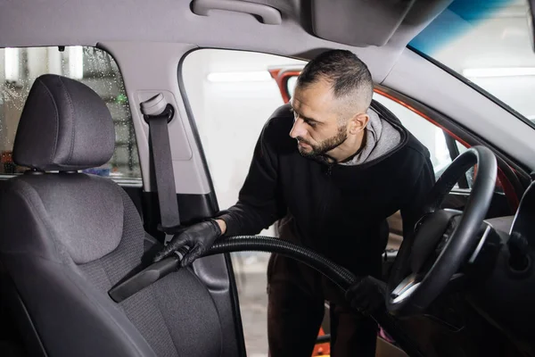Details of car vacuum cleaning. Professional young male worker using vacuum cleaner for dirty car interior. Auto car service worker using vacuum cleaner to wash car seat.