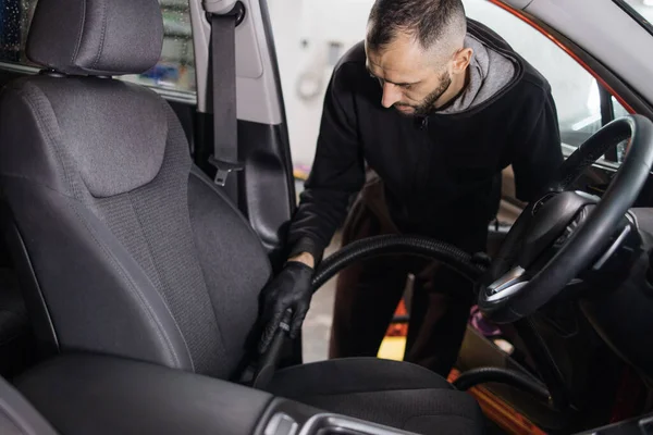Details of car vacuum cleaning. Professional young male worker using vacuum cleaner for dirty car interior. Auto car service worker using vacuum cleaner to wash car seat.