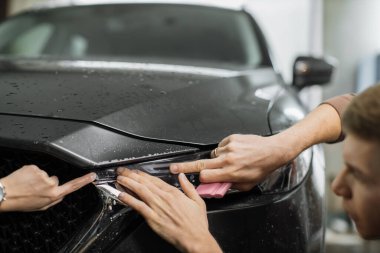 Modern lüks arabanın ön farındaki koruma film kurulumunu kapatın. PPF, araba yüzeyine uygulanan poliüretan film boyayı taş parçalarından, böcek sıçramalarından ve aşınmadan korumak için..