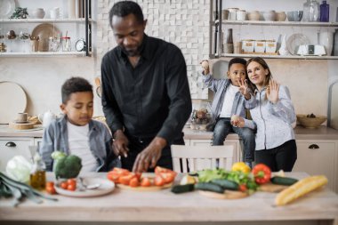 Kafkasyalı anne ve tatlı Afrikalı anaokulu çocuğu haftasonu mutfakta rahatlarken eğleniyorlar, ilgili baba küçük çocuğa yemek yapmayı öğretiyor, salata için sebze doğramaya yardım ediyor, aile hafta sonu konsepti..