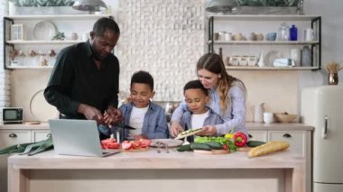 Mutlu Afrikalı şirin çocuklar ve genç ebeveynleri dizüstü bilgisayarlarında birlikte yemek pişiriyorlar taze sebze ve salata yapıyorlar, mutfakta yemek yapıyorlar..