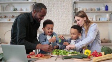 Mutlu ebeveynler ve oğulları mutfakta yemek pişirip birlikte salata hazırlıyorlar. Mutlu çocuklar anne ve babaya yardım eder, akşam yemeği ya da öğle yemeği için yardım eder, marul yapraklarını kaseye atar..