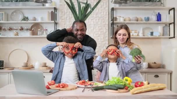 キッチンで料理を楽しみながら 幸せな興奮した両親と息子の子供たちを笑顔 面白いお母さん お父さんと子供たちは コショウスライスグラスを作り サラダ用の野菜を切ります 家で食べる家族 — ストック動画
