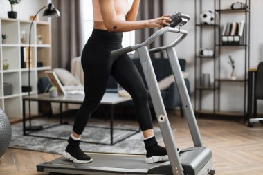Cropped view of hands and legs of young sporty african woman having working out using treadmill in the morning at home gym. Concept of sports, activity, healthy lifestyle.