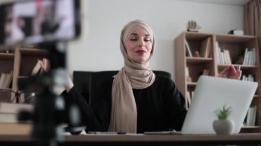 Muslim woman freelancer sitting at table with closed eyes recording blog how to relieving stress by meditation at workplace. Concept of relaxation and harmony, no stress free relief at work.