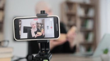 Focus on smart phone screen, muslim woman doing live stream while unpacking box with new smart watch. Female blogger sharing her feedback about modern gadget with her subscribers.