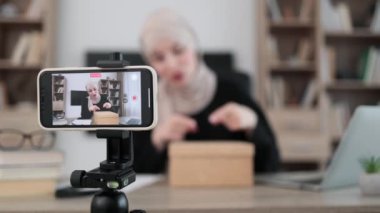 Focus on smart phone screen, pleasant arab woman filming video on modern phone camera while opening parcel box. Concept of people, technology and blogging.