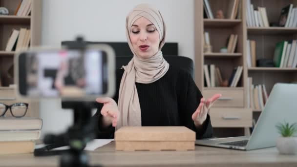 携帯電話のカメラでビデオを記録するイスラム教徒の女性は 新しいワイヤレスタブレットで箱を開梱しながら 新しい注文についての肯定的なフィードバックを加入者と共有する女性インフルエンサー — ストック動画