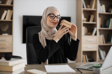 First person view of muslim female blogger opening gift box while sitting at home. Positive young woman doing live stream during unpacking process.