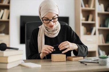 Muslim woman doing live stream while unpacking box with new smart watch. Female blogger sharing her feedback about modern gadget with her subscribers.
