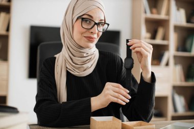 Arabian female blogger sharing her feedback about modern gadget with her subscribers. Muslim woman doing live stream while unpacking box with new smart watch.