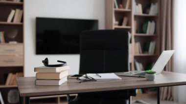 Shot of modern workplace, office with laptop, books, papers, eyeglasses, headset on wood table with large tv on white wall background.