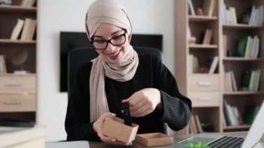 Muslim woman doing live stream while unpacking box with new smart watch. Female blogger sharing her feedback about modern gadget with her subscribers.