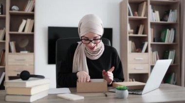 Muslim woman doing live stream while unpacking box with new smart phone. Female blogger sharing her feedback about modern gadget with her subscribers.