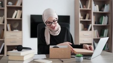 Arabian female blogger sharing her feedback about modern gadget with her subscribers. Muslim woman doing live stream while unpacking box with new headphones.