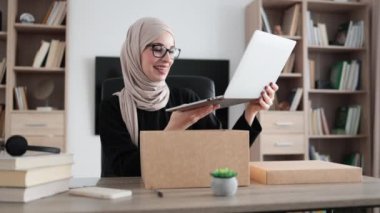 Muslim woman doing live stream while unpacking box with new laptop. Female blogger sharing her feedback about modern gadget with her subscribers.