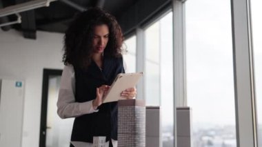 İnsanlar, küresel iş, şirket çalışanı konsepti. Tablet kullanarak resmi kıyafetlerle gülümseyen kıvırcık saçlı kadının portresi, 3D şehir modelinin kompleks prototip projesinin önünde poz veriyor..