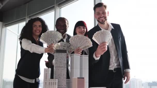 由多种族商人组成的团队 手握一捆美圆现金 与3D摩天大楼模型在办公室的内部保持着接近餐桌 全景尽收眼底 — 图库视频影像