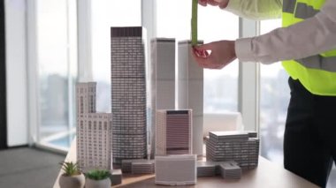 Cropped view of hands of engineer working on building complex prototype project of residential or business district, measuring city model using ruler at office with panoramic windows