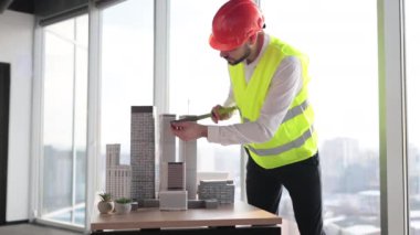 Sakallı, koruyucu miğfer mühendisi, panoramik pencereli cetvel kullanarak şehir modelini ölçerek, konut ve iş bölgesinin kompleks prototip projesi üzerinde çalışıyor.