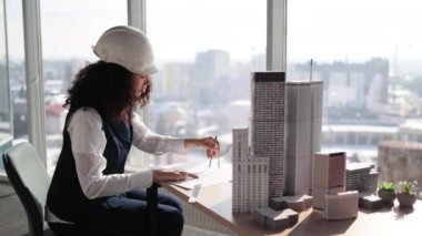 Konut ve iş alanlarının kompleks prototip projesi üzerinde çalışan kıvırcık kadın mühendis, panoramik pencereli pusula kullanarak şehir modelini ölçüyor