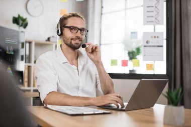 Positive caucasian male office manager in white shirt writing financial report using wireless laptop computer during working online. Online communication concept.
